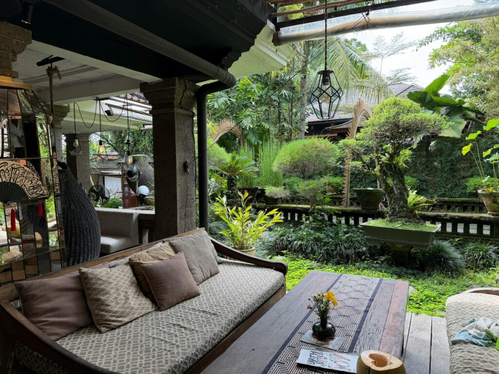 Outdoor covered patio with a cushioned wooden sofa and coffee table, overlooking a lush garden—showcasing inviting hardscaping ideas for backyard relaxation among vibrant plants and trees.