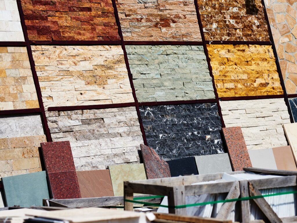 Various types and colors of stone tiles are displayed vertically in organized rows, offering inspiring hardscaping ideas for backyard projects, with some construction materials visible in the foreground.