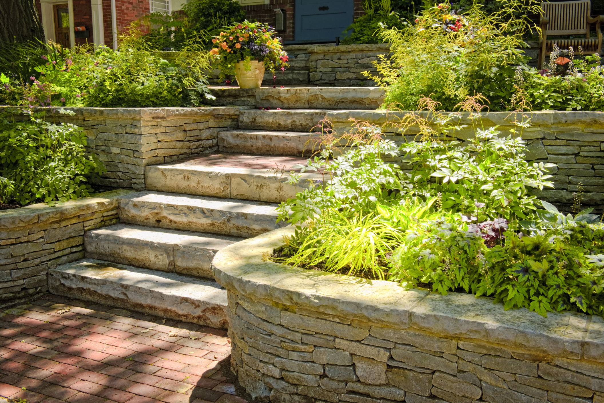 Stone steps and retaining walls with lush green plants and flowers in a landscaped garden.