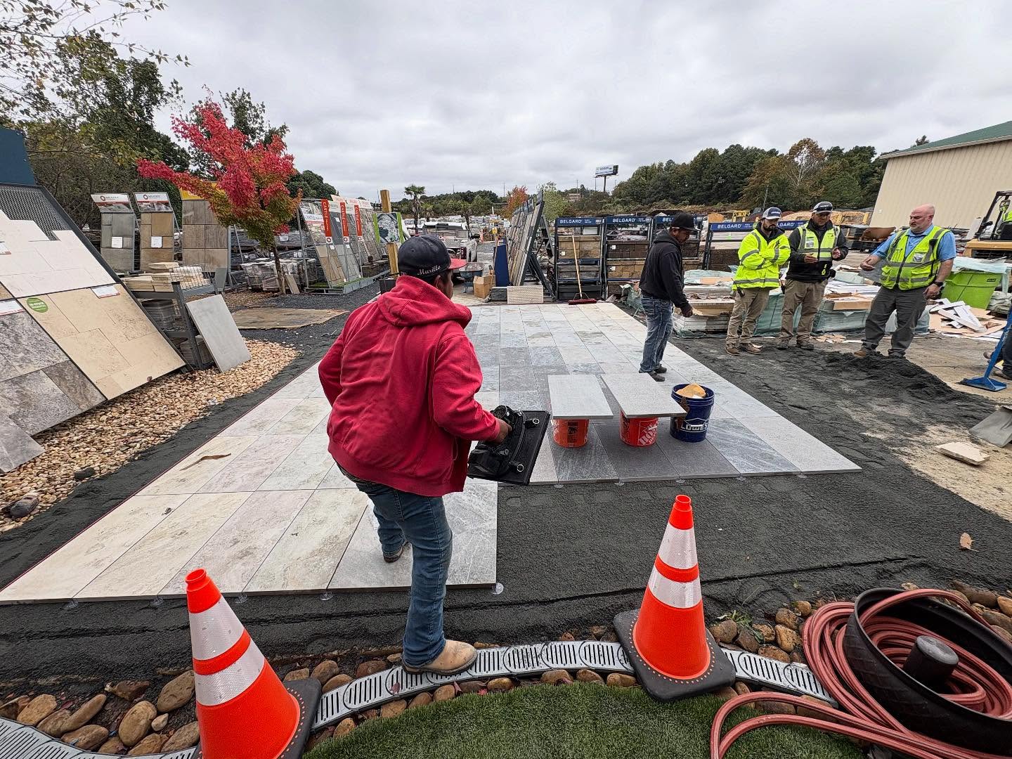 Workers installing large stone tiles outdoors as part of our process, with safety cones, tools, and construction materials visible around the site.