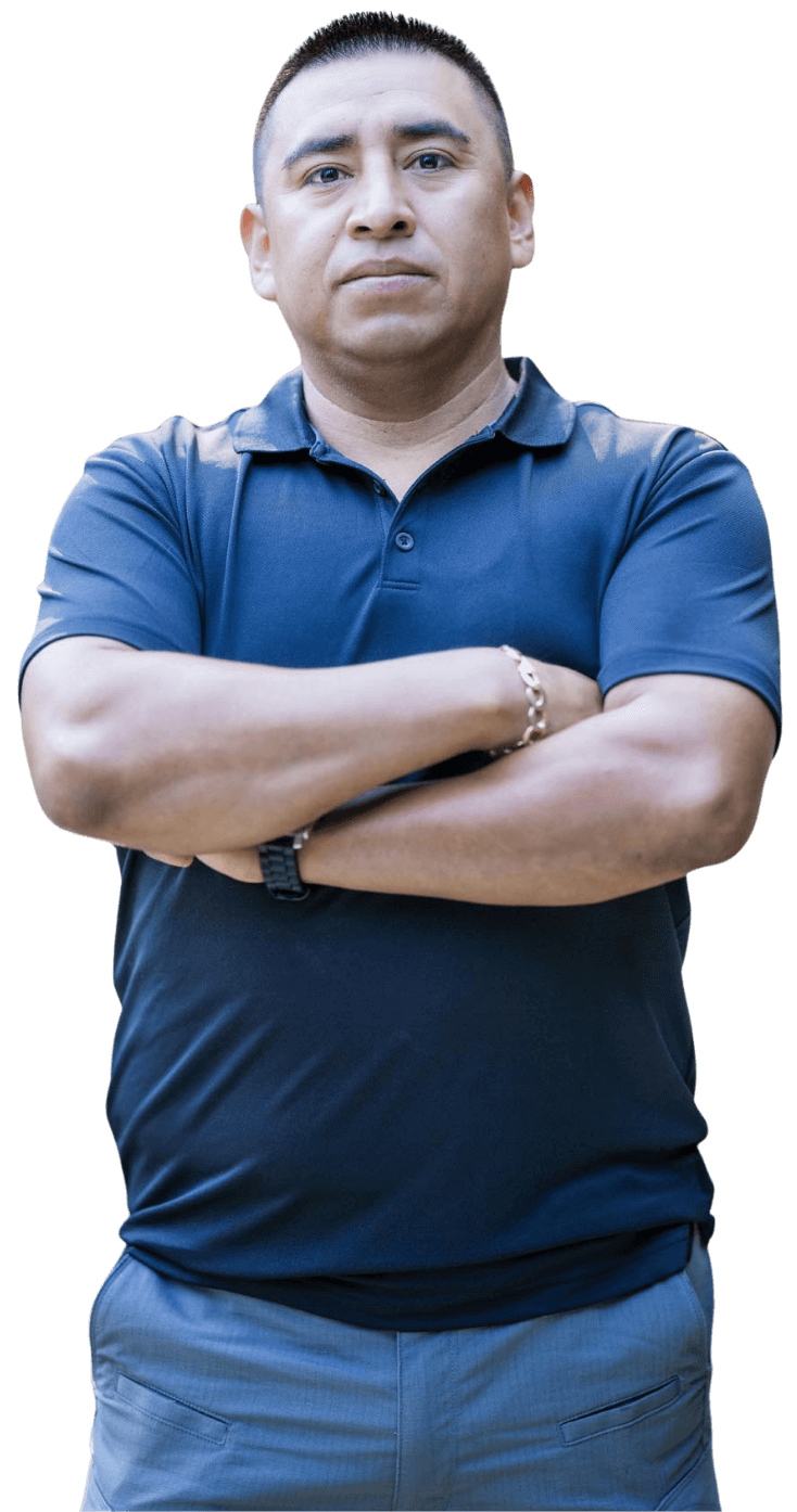 A man in a navy blue polo shirt and gray pants stands with his arms crossed, looking at the camera against a plain white background.