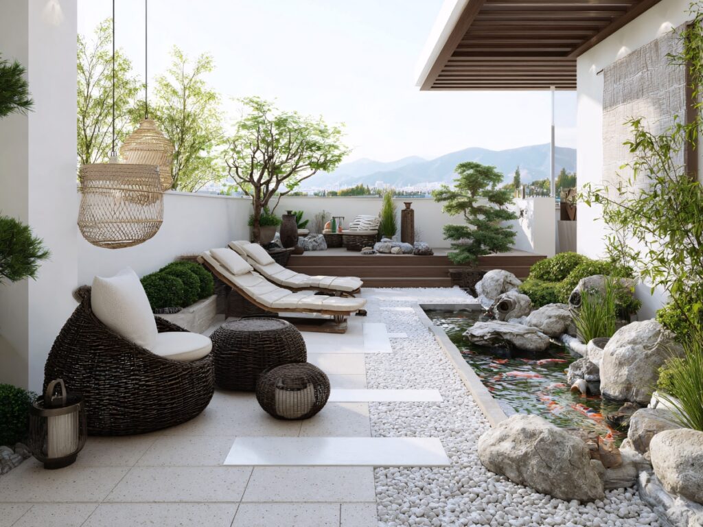 A modern rooftop outdoor space with lounge chairs, wicker furniture, a koi pond, lush green plants, white gravel, and mountains visible in the background.
