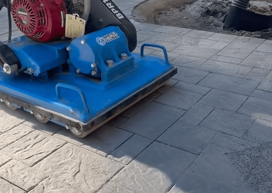 Plate compactor flattening and smoothing stone pavers during a paver patio and paver installation process, ensuring a level and durable patio surface.