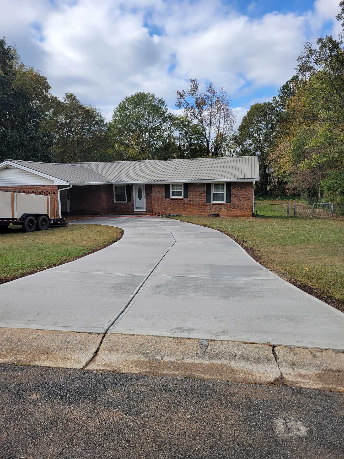 Concrete driveway installation with a smooth finish, leading to a brick home, surrounded by green grass and trees, showcasing enhanced curb appeal and functionality.
