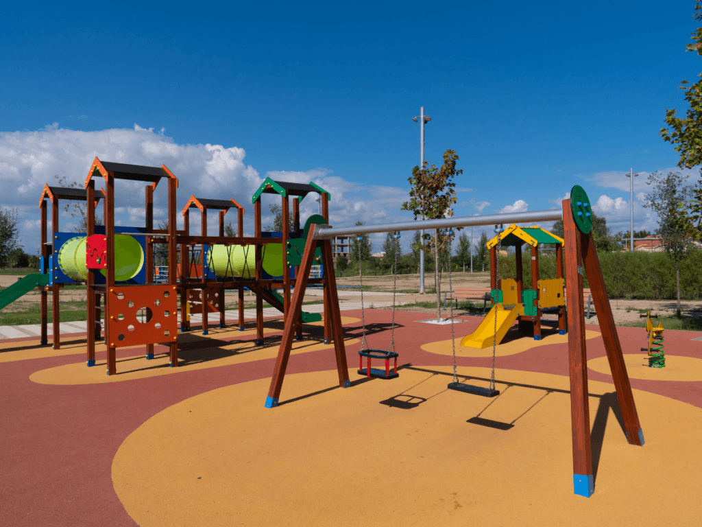 Outdoor playground with climbing structures, slides, swings, and tunnels on a rubberized safety surface under a clear blue sky—perfect for kids play areas.