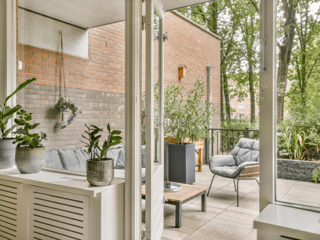 A modern patio with outdoor seating, potted plants, and a brick wall offers great small yard solutions, all seen through open glass doors from inside the home.